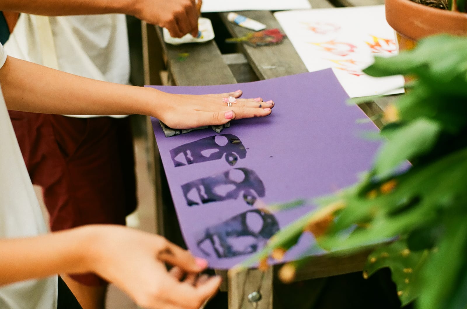 Summer Camp, 2015 — a hand presses a foam stamp onto purple paper, three printed faces in a row